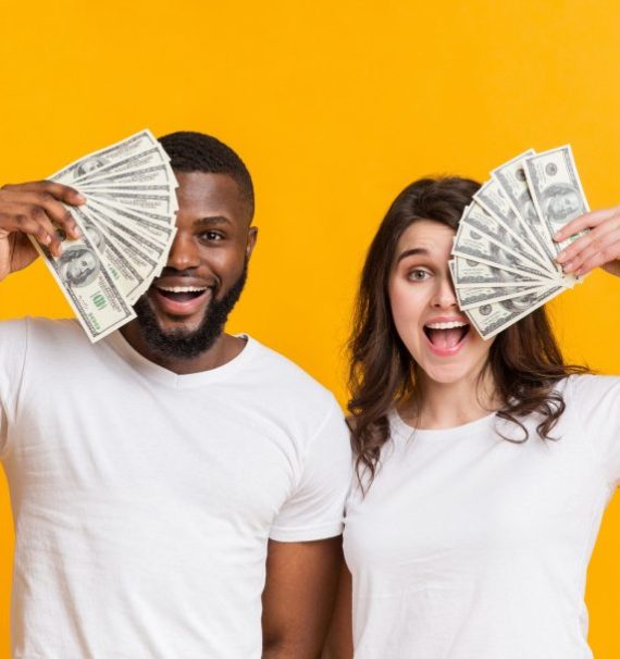 Excited multiracial couple covering eyes with dollar cash fan
